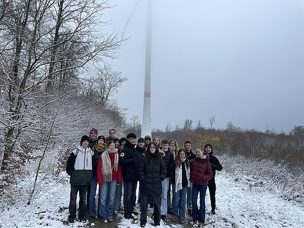 Gruppe von Jugendlichen steht vor einem Windrad im Schnee. Gruppe von Menschen im Schnee nahe Windrad.