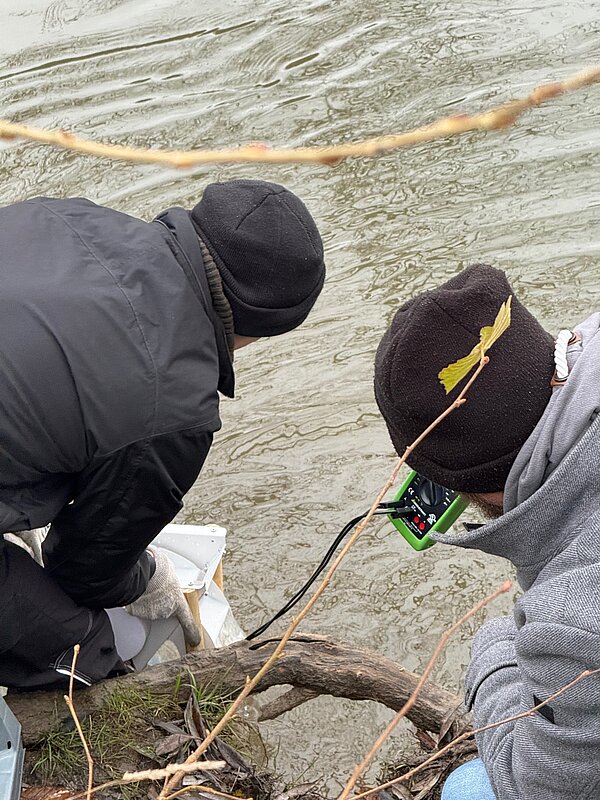 Zwei Personen testen die Wasserqualität an einem Gewässer. Menschen messen Wasserqualität.