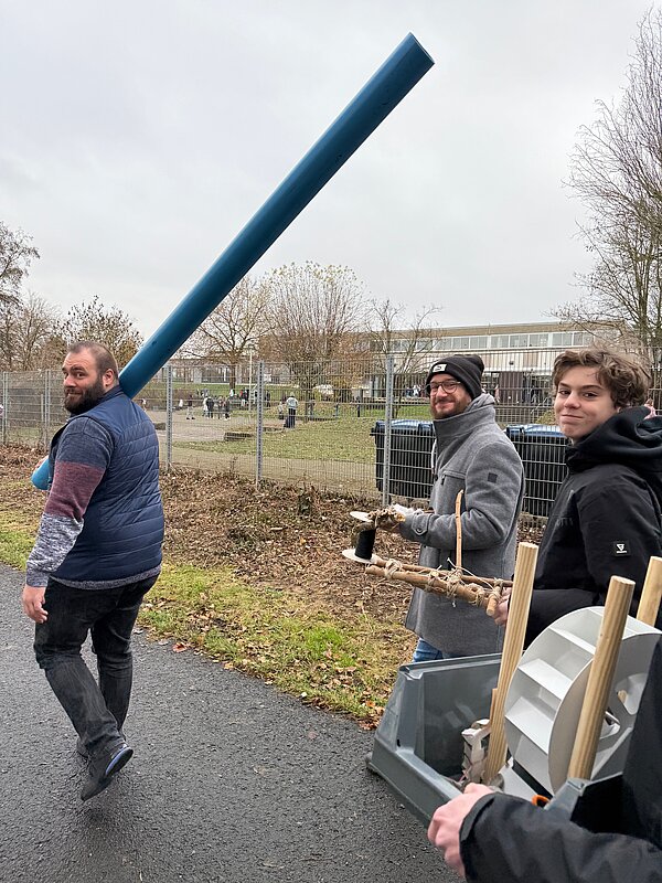 Drei Männer tragen Bastelmaterialien im Freien Drei Männer mit Bastelmaterialien