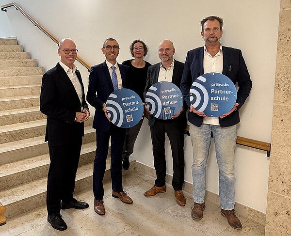 Fünf Personen auf einer Treppe mit Partnerschul-Schild Gruppe von fünf Personen mit Schildern