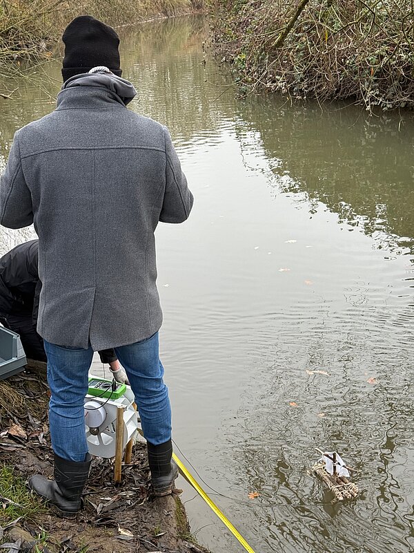 Eine Person untersucht das Wasser an einem Gewässer Person am Ufer eines Gewässers